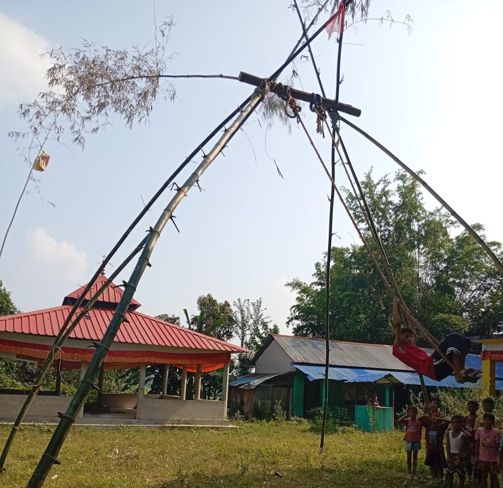 Students playing on a traditional bamboo swing (Linge Ping) at Narmadeshwar Aadarsha Sanskrit Bidyapheet Gurukul during a festival celebration.